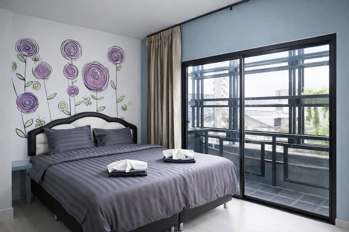 A modern bedroom with a large bed, a view of the city through a balcony, and a wall with floral artwork.
