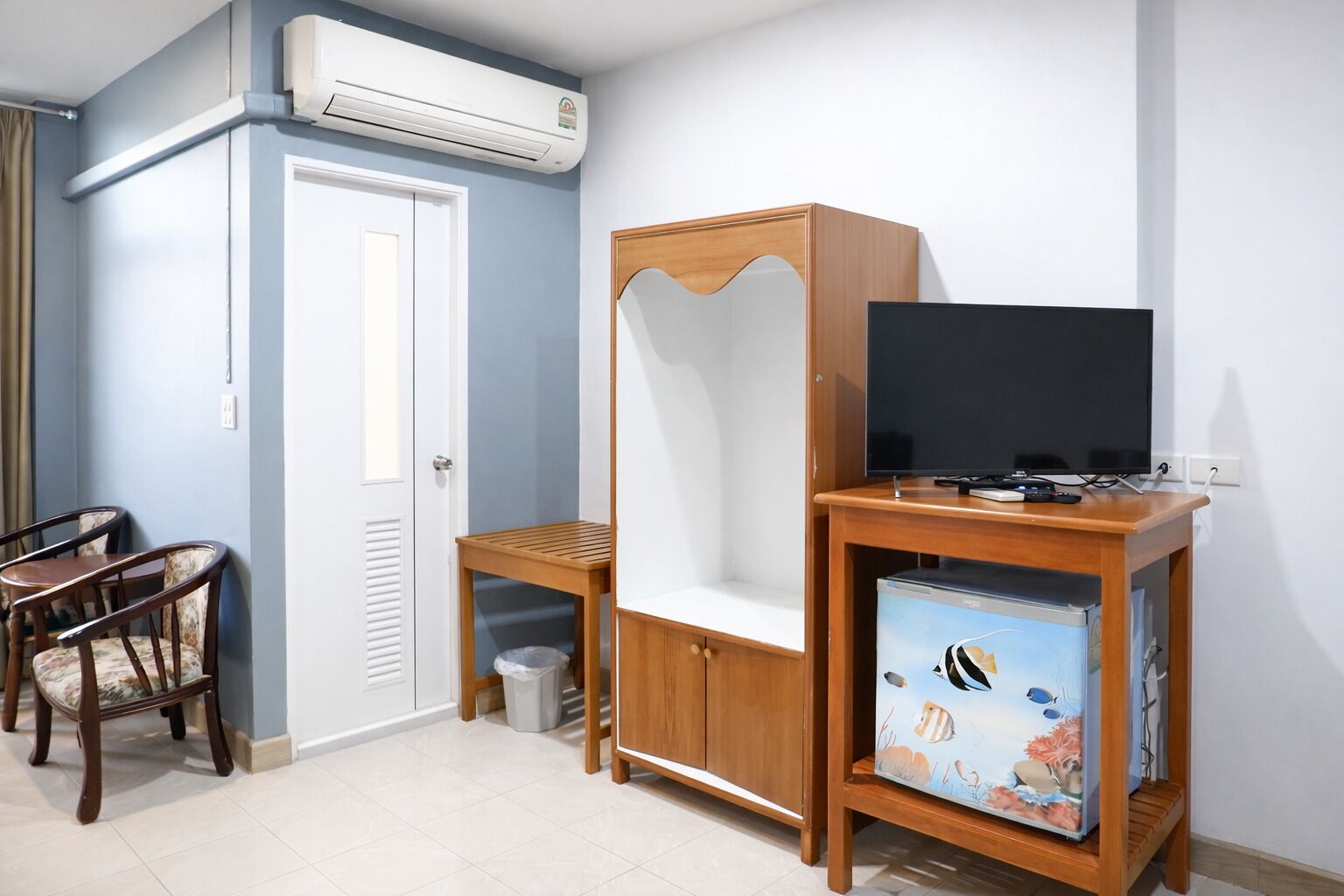 Une pièce comprenant un lit, un bureau avec une chaise, un téléviseur posé sur un meuble en bois et un climatiseur fixé au mur.