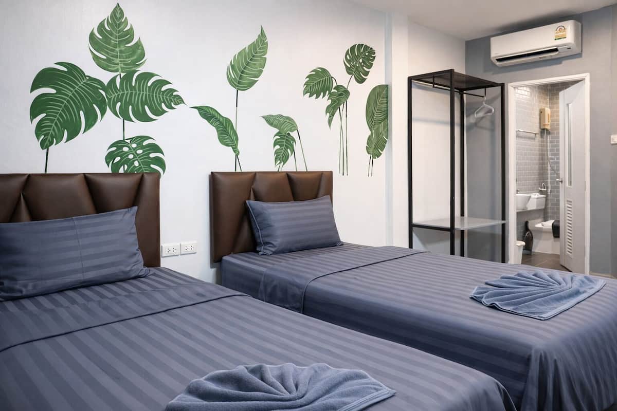 A hotel room with two beds, a shower, and a wall with large green leaf decorations.