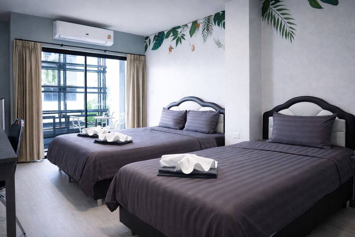 A hotel room with two beds, a desk, and a window with curtains.