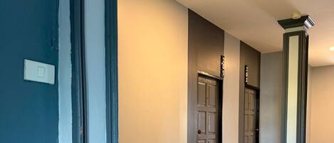 A hallway with a wooden floor, a green exit sign, and a door with a number above it.