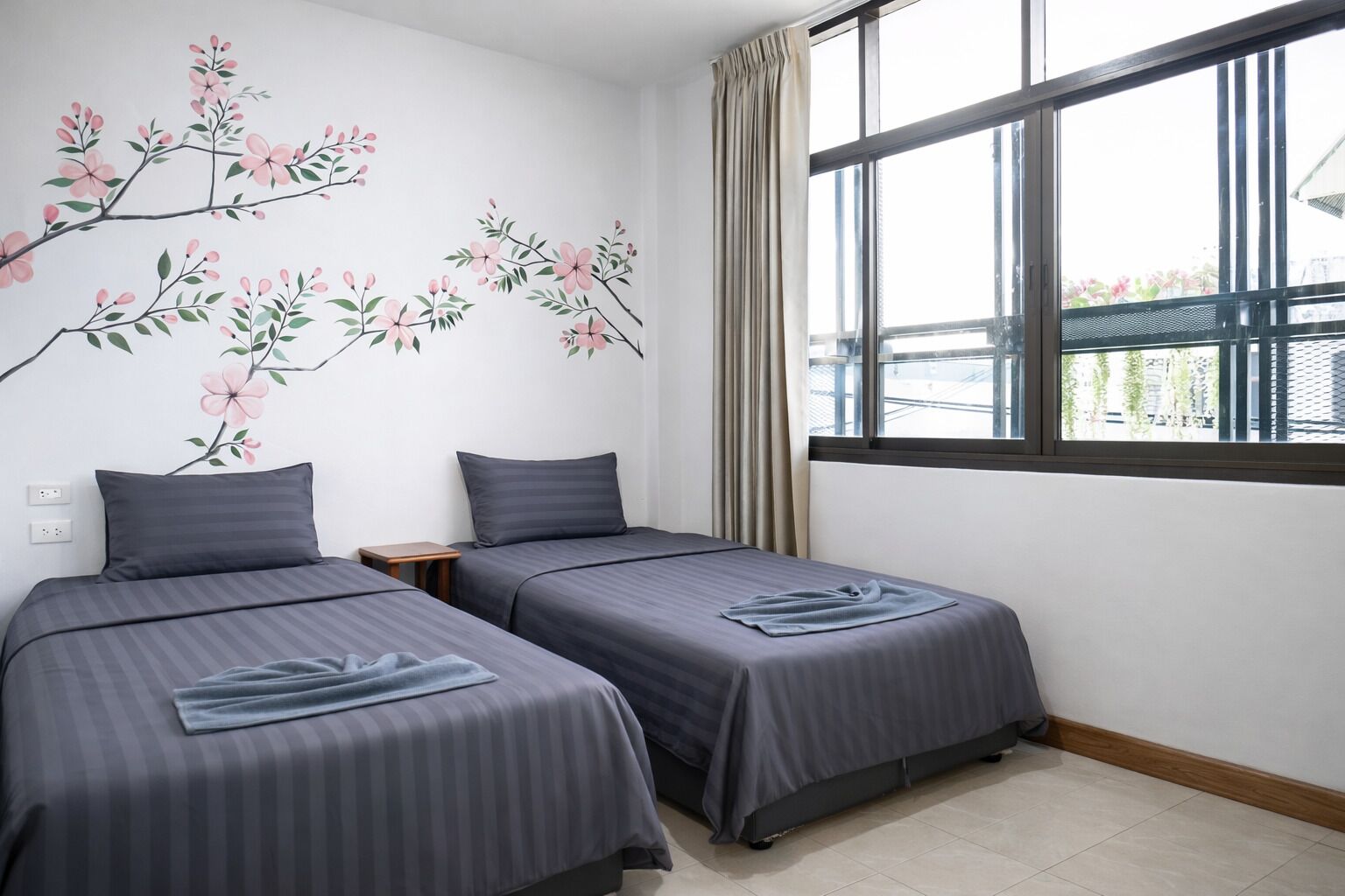 A hotel room with two beds, a window with curtains, and a wall with a floral mural.