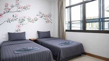 A hotel room with two beds, a window with curtains, and a wall with a floral mural.