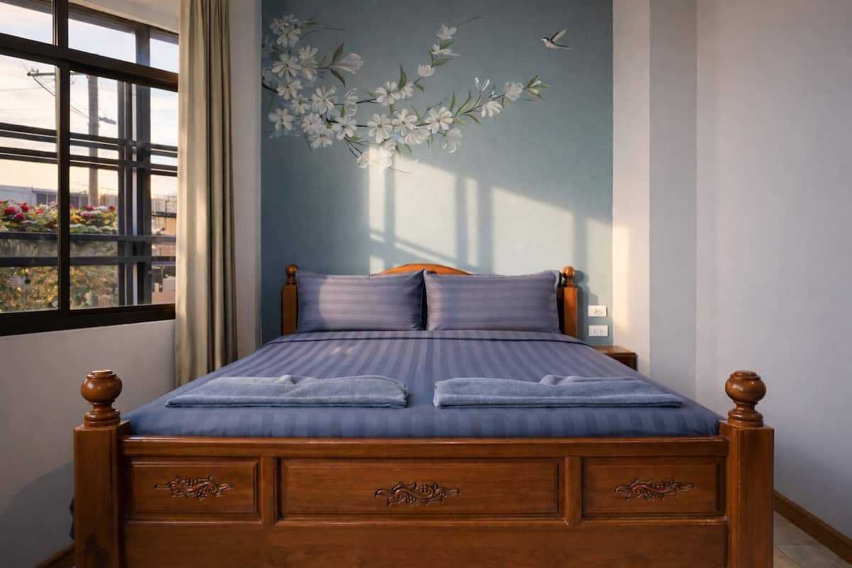 A bedroom with a bed, wooden headboard, and a window with a view of greenery.