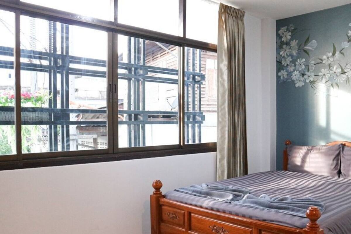 A bedroom with a bed, a window with a view of buildings, and a wall with a floral mural.