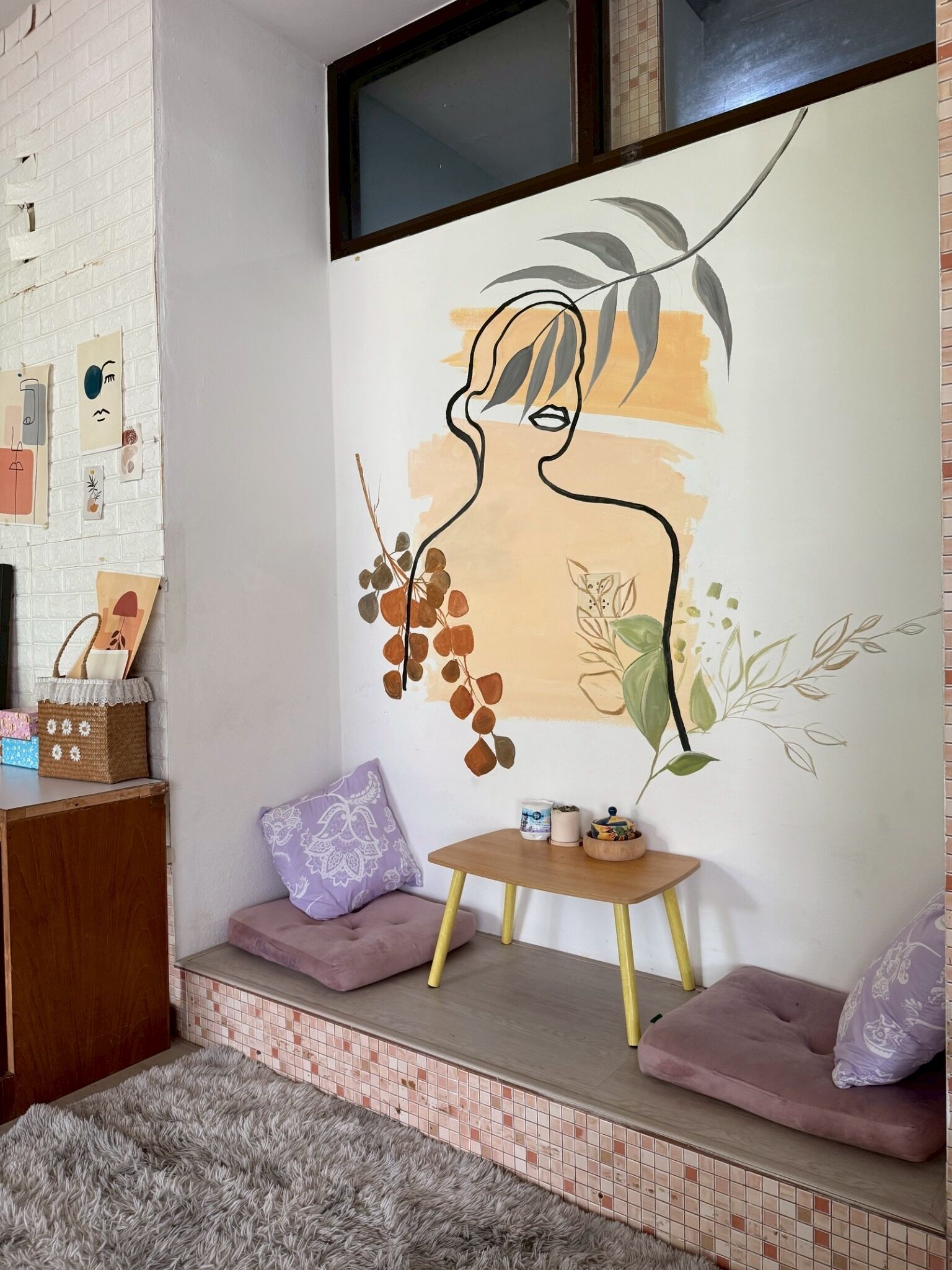 A room with a white brick wall, a large abstract painting, a small wooden table, and a cushioned bench.