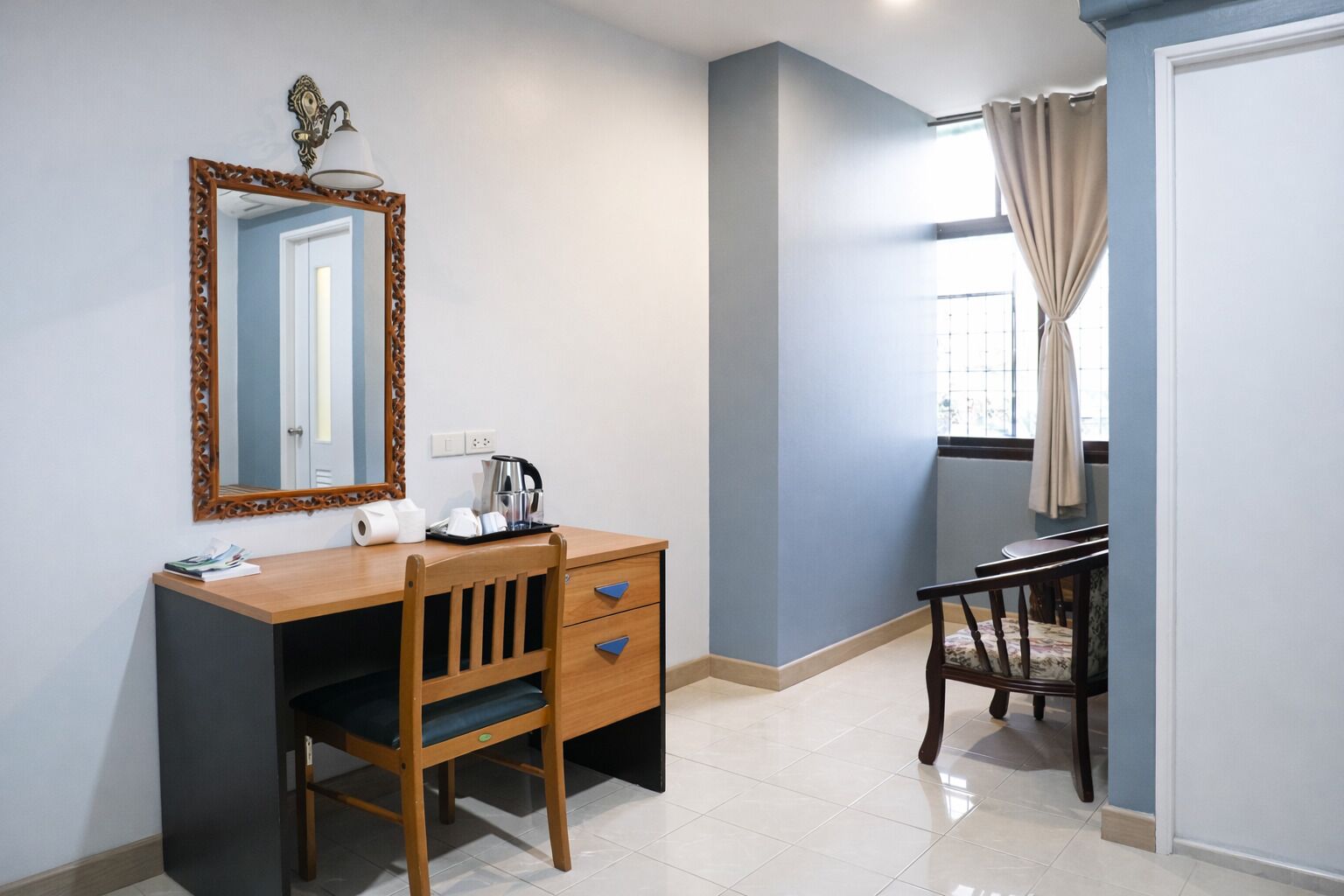 A room with a wooden desk, a chair, a mirror, a window with curtains, and a light fixture.