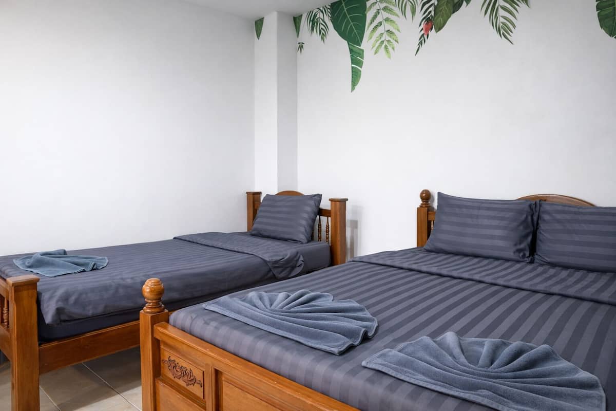 Two wooden beds with grey bedding and blue towels, white walls, and a plant decoration.