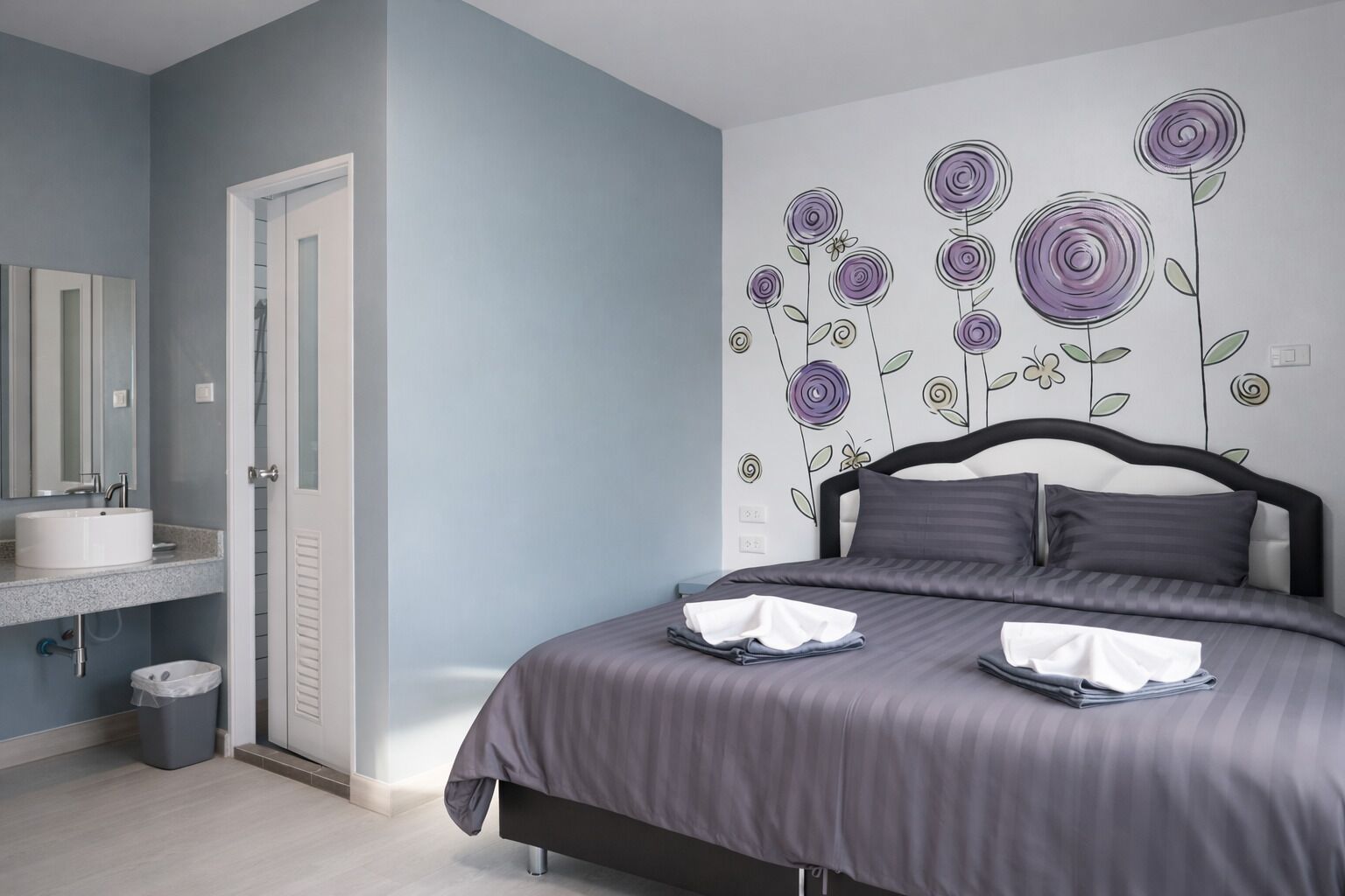 A bedroom with a bed, a bedside table, a mirror, and a wall with floral wall art.