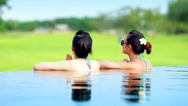 Two people relaxing in a swimming pool with a green landscape in the background. - Uniland Golf & Resort (Nakhon Pathom)