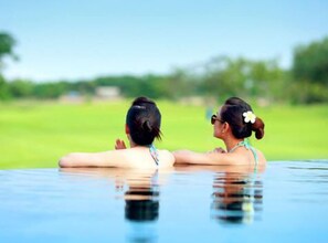 Dos personas descansando en una piscina con un paisaje verde de fondo.