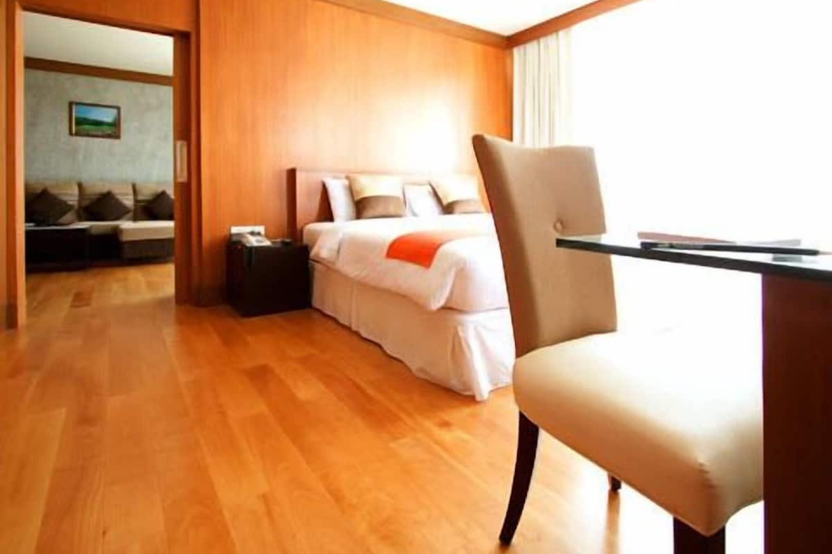Une chambre d’hôtel avec un plancher en bois, un lit avec une literie blanche et un plaid orange, un bureau avec une chaise, et une vue sur l’extérieur.