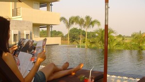 A person reading a magazine by a pool with a drink on the table. - Uniland Golf & Resort (Nakhon Pathom)