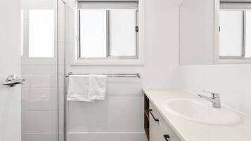 Un bagno moderno con cabina doccia in vetro, lavandino bianco e finestra sopra lo specchio.