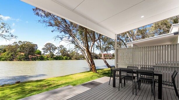 A covered outdoor area with a wooden deck, black metal chairs, and a view of a lake and trees. - Echo Holiday Parks - Renmark (Renmark)