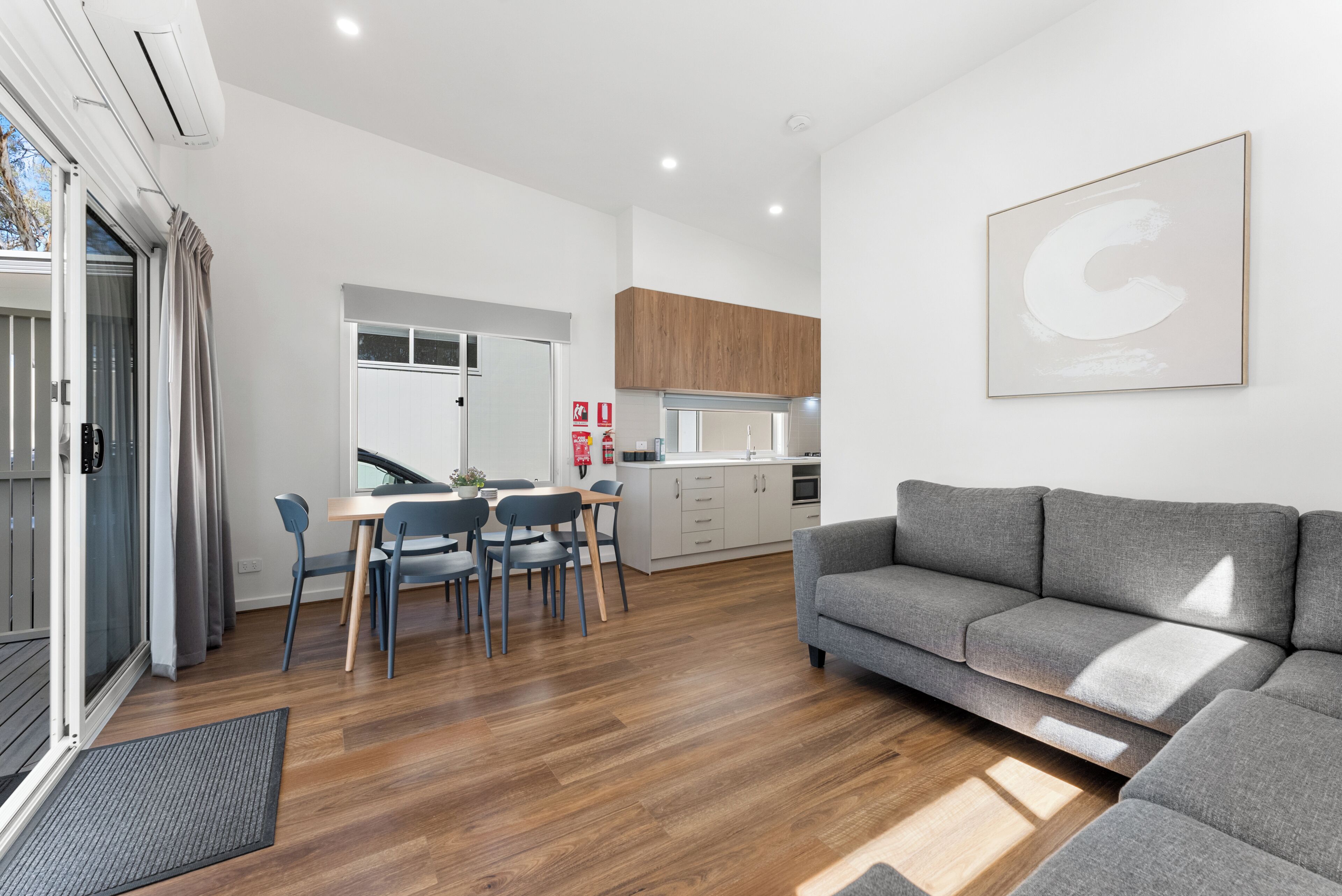 Un salón moderno con un sofá gris, suelo de madera y un comedor con sillas y una mesa.