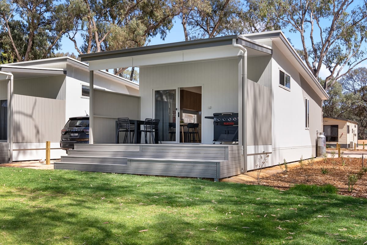 A modern mobile home with a covered patio, a barbecue grill, and a small deck area.