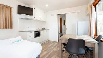Ein kompaktes Hotelzimmer mit Bett, einer Küchenzeile, einem Esstisch mit Stühlen und einem Fernseher, der über dem Tresen angebracht ist.