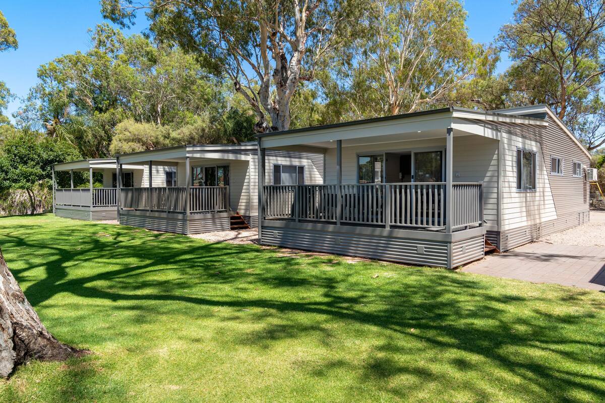 A row of mobile homes with attached porches, surrounded by a grassy area and trees.