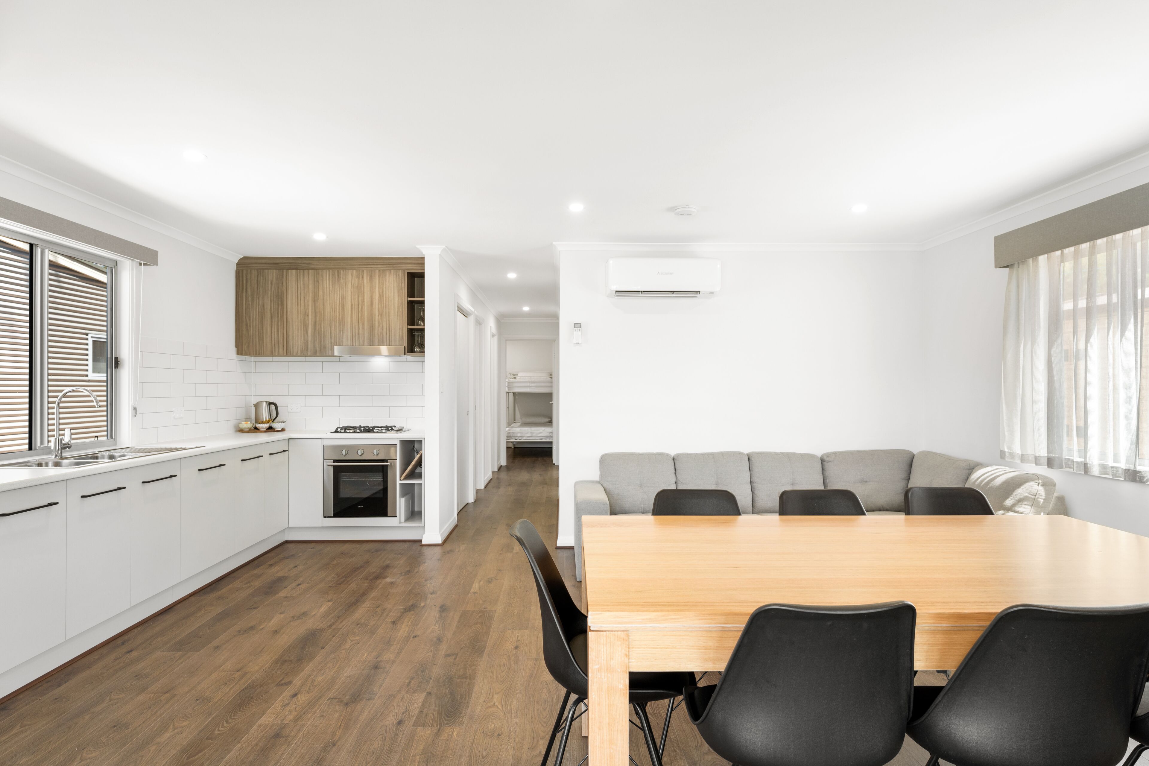 A modern kitchen with white cabinets, a wooden dining table, and a gray sofa in the dining area.