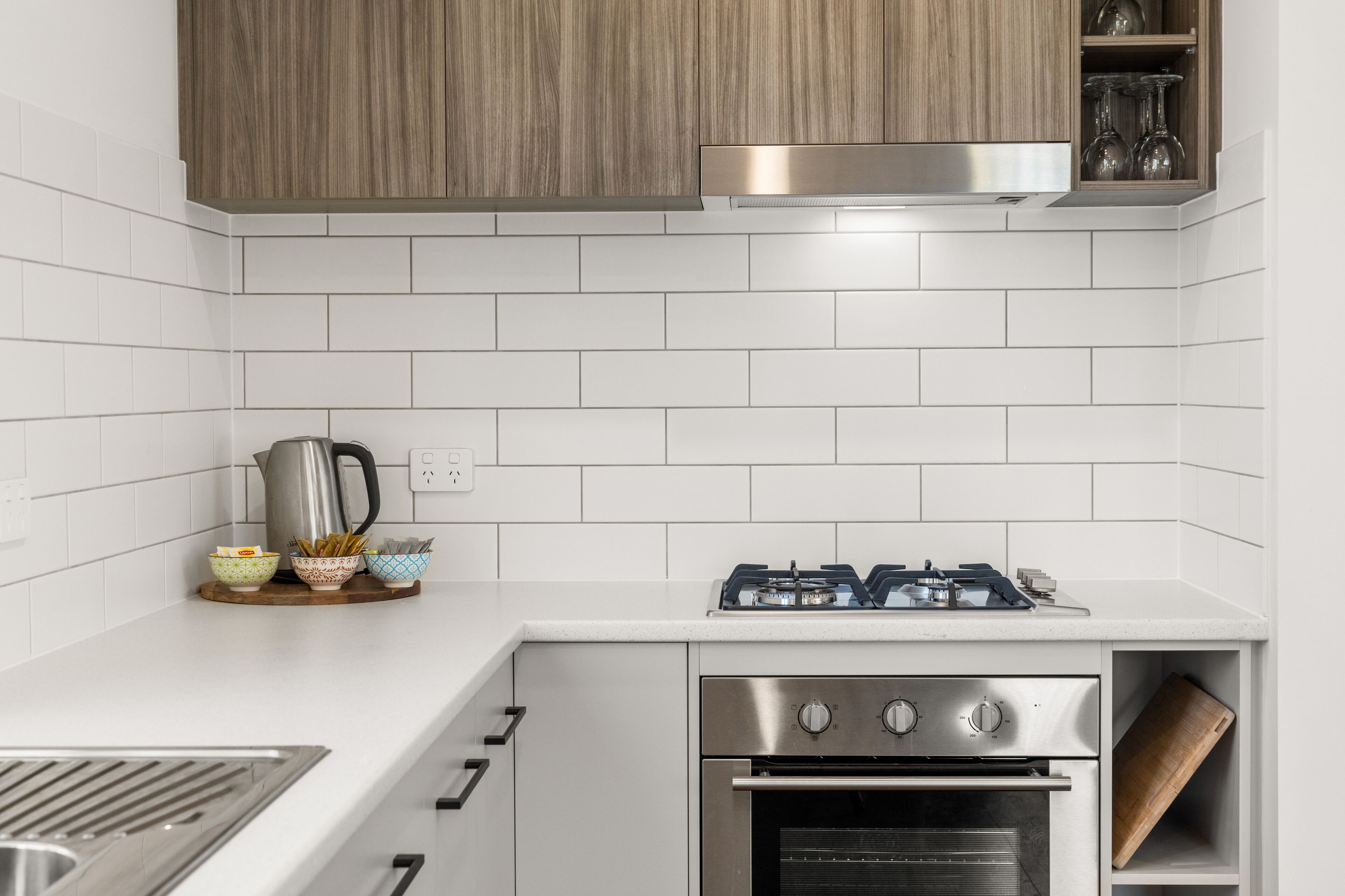 Una cocina moderna con azulejos blancos tipo metro, electrodomésticos de acero inoxidable y armarios de madera.