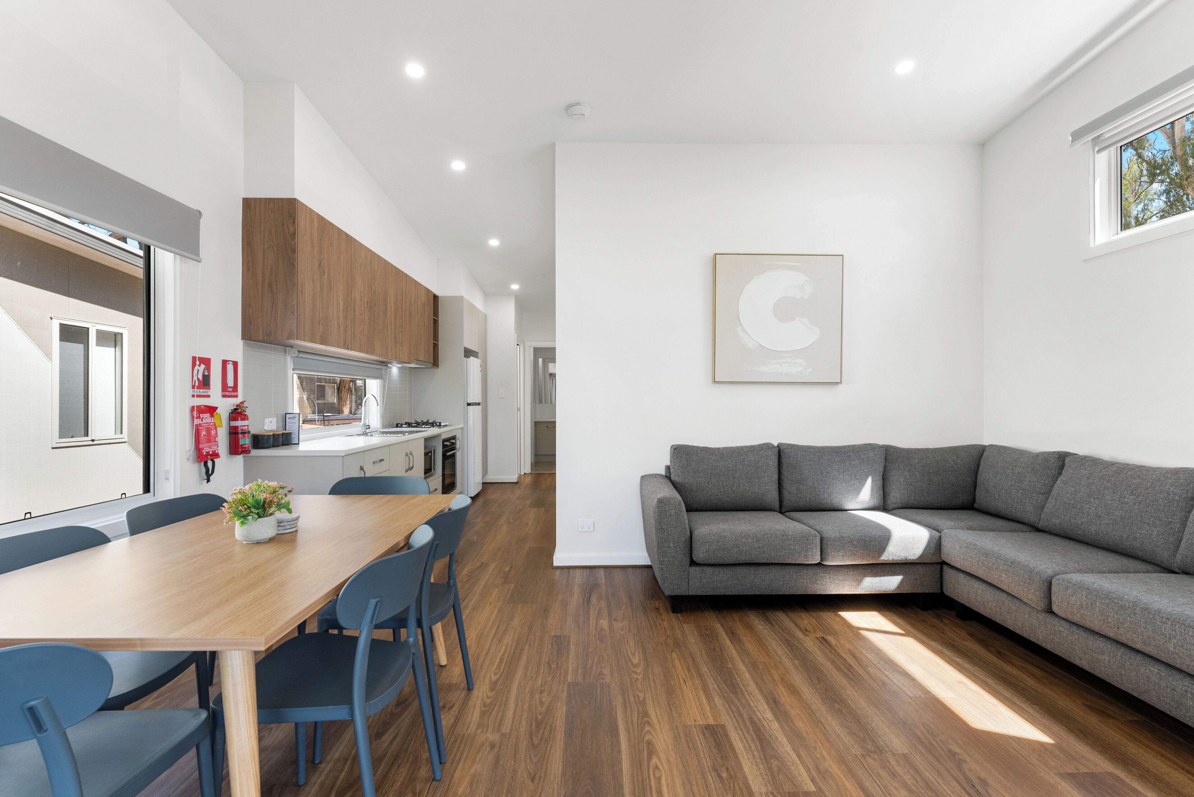 A modern kitchen with wooden cabinets, a dining table with chairs, and a gray sectional sofa.