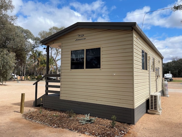 A small, single-story mobile home with the brand name 'Jayco' on the front. It has a small porch with a wooden bench and a single window on the side. - Echo Holiday Parks - Renmark (Renmark)