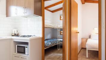 A compact room with a kitchenette, a bunk bed, and a small bedside table.