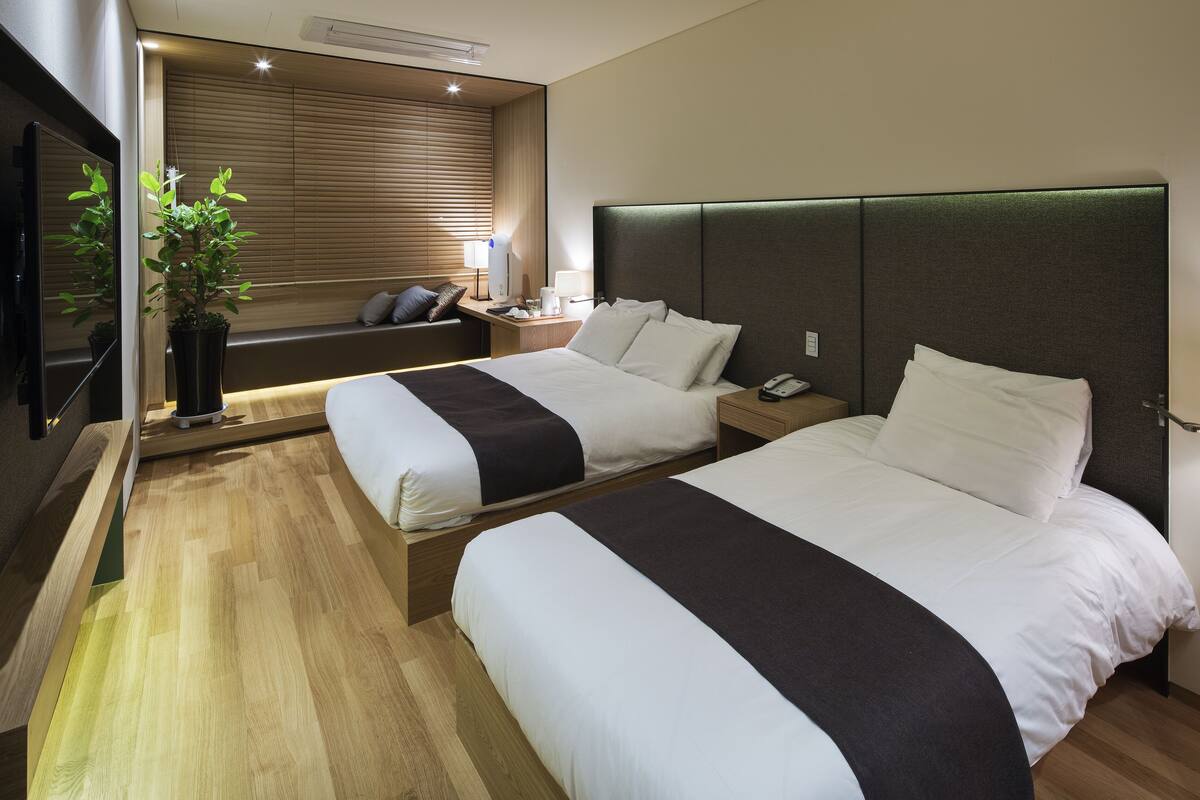 A hotel room with two beds, a seating area with a plant, and a TV.