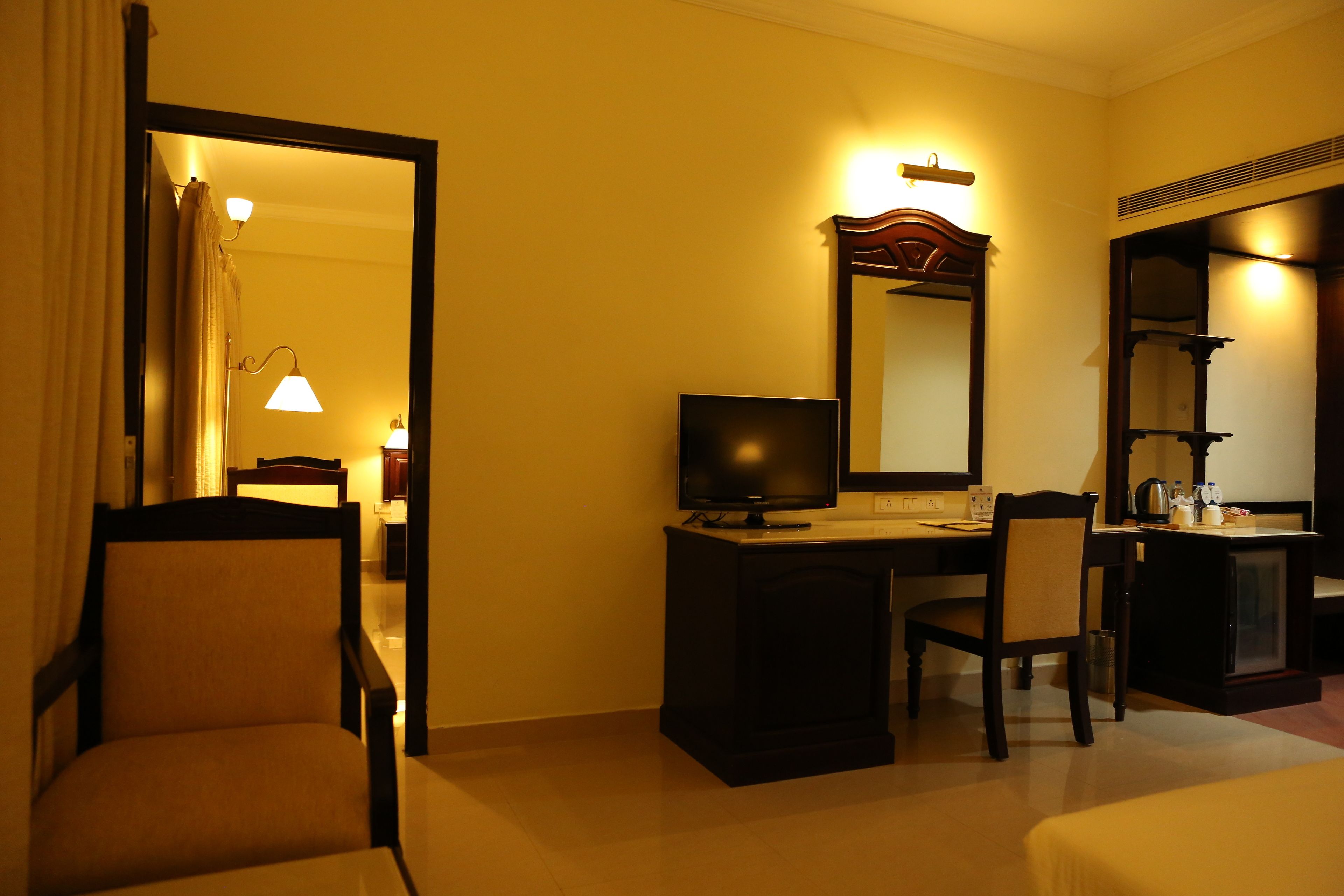 A hotel room with a desk, a chair, a bed, a television, and a mirror.