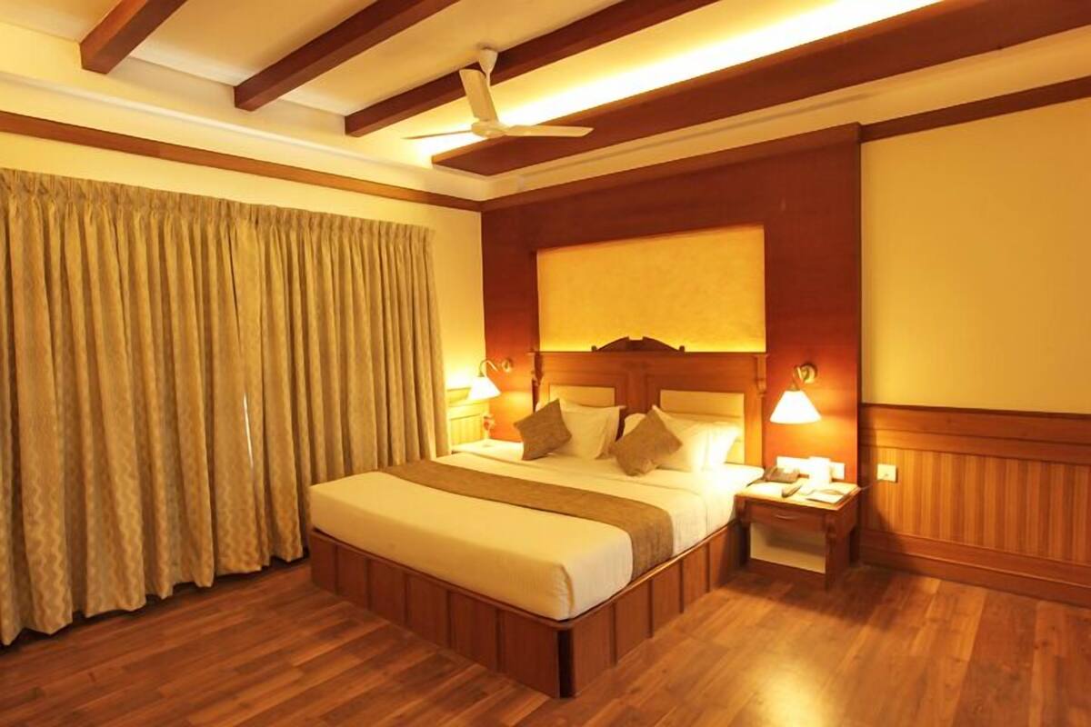 A hotel room with a large bed, wooden flooring, a ceiling fan, and two bedside lamps.