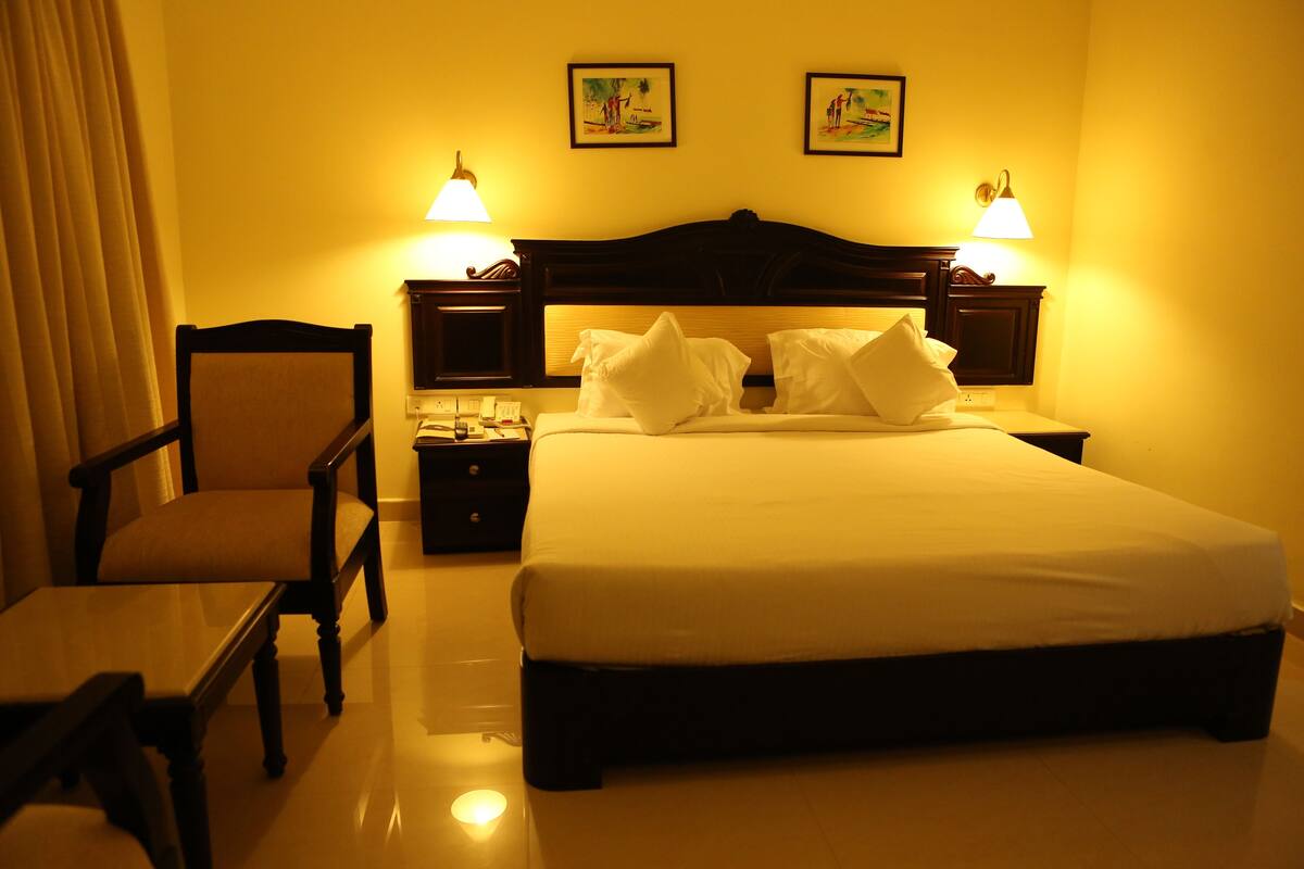 A hotel room with a bed, a chair, a nightstand, and two wall-mounted lamps.