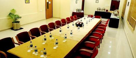Una sala de conferencias con una larga mesa, sillas rojas y botellas de agua.