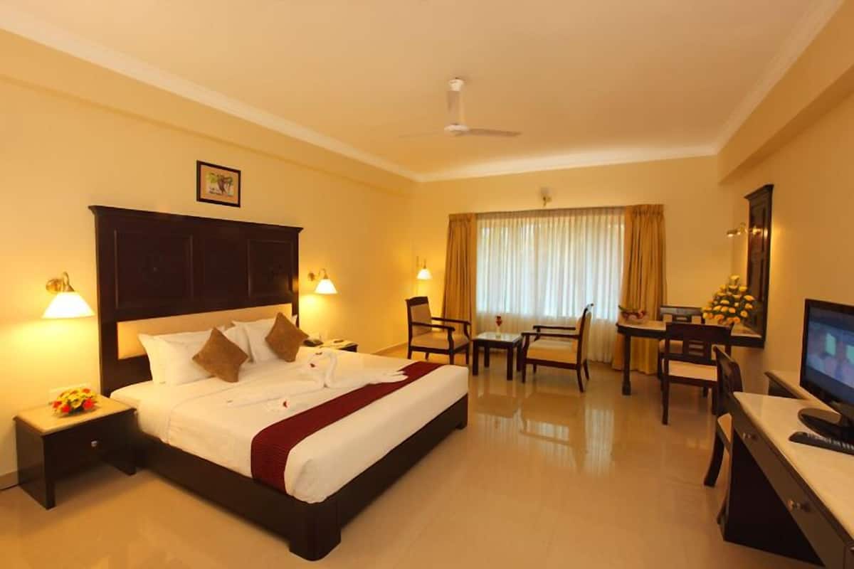 A hotel room with a large bed, bedside tables, a desk with a chair, a television, and a window with curtains.