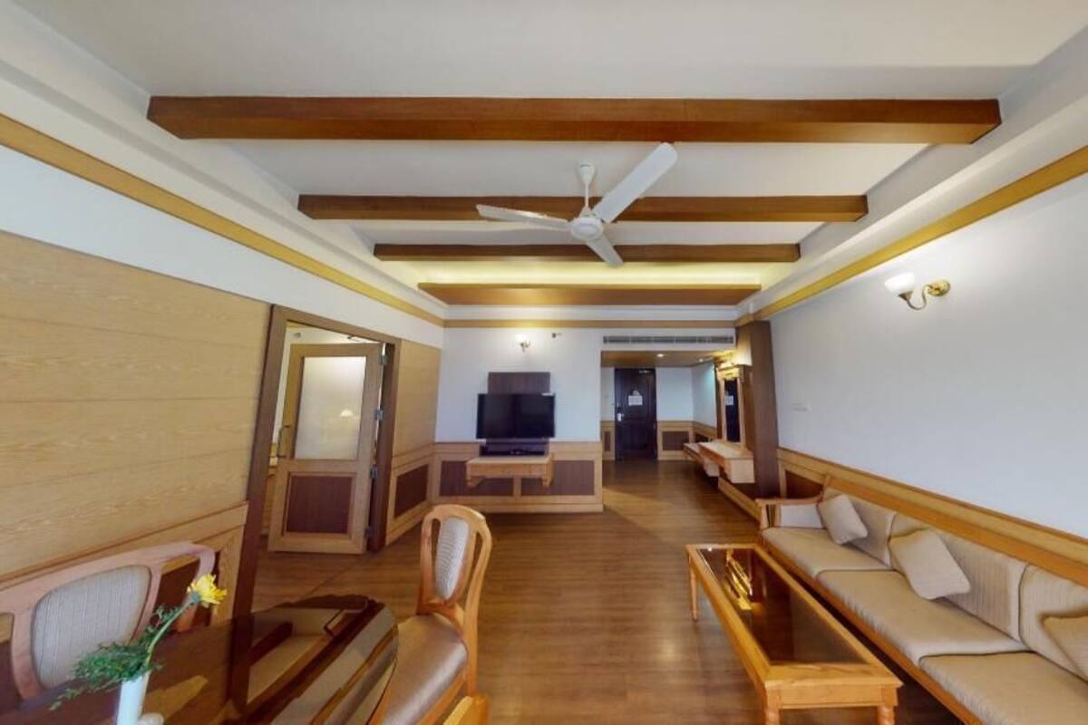 A spacious living room with wooden beams, a ceiling fan, a sofa set, and a television.