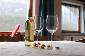 A table with a bottle and two glasses, a red chair, and a view of a forest through a window.
