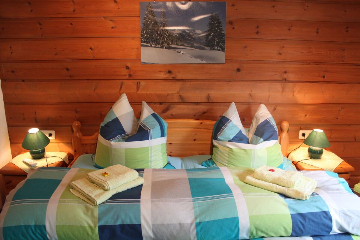 A wooden cabin bedroom with a bed, pillows, and a nightstand with a lamp.