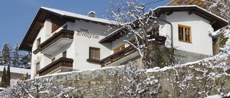 A two-story building with a stone wall and a balcony. The building has a sign that reads "Haus Evelyn."