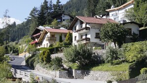 Una zona residencial en una ladera con casas que tienen balcones, una calle pavimentada y un muro de contención de piedra.