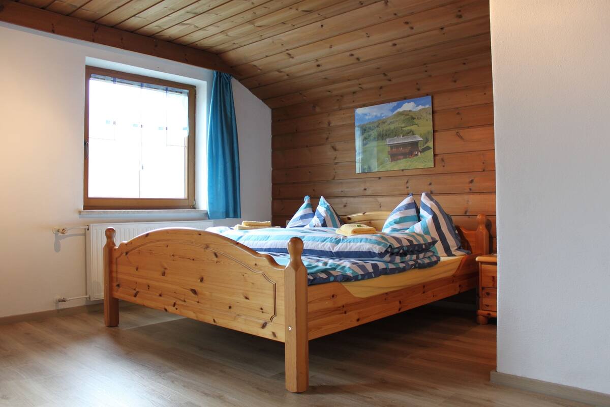 A wooden bed in a room with a window and a painting on the wall.