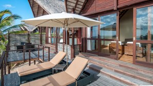 Eine Holzterrasse mit Liegestühlen und Sonnenschirm, mit Blick auf einen Poolbereich.