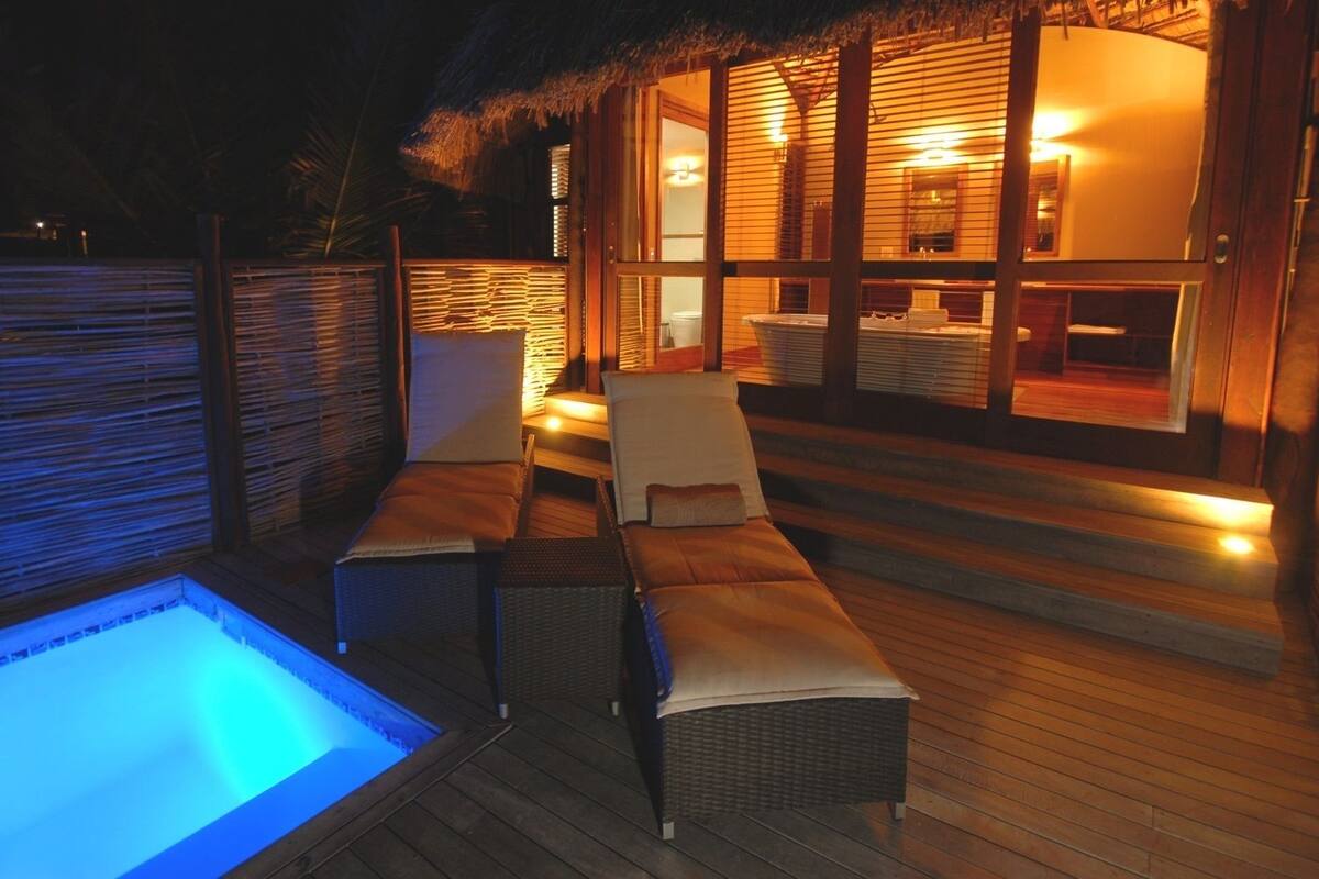 Un espacio exterior bien iluminado con piscina, sillones de descanso y una terraza de madera.