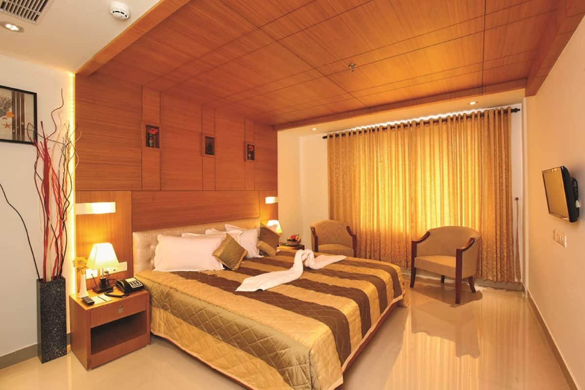 Une chambre d’hôtel avec un plafond en bois, un grand lit recouvert d’une courtepointe à rayures, un coin salon avec un fauteuil et une table de chevet avec une lampe et un téléphone.
