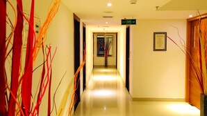A hotel corridor with a polished floor, an exit sign, and a framed document on the wall.