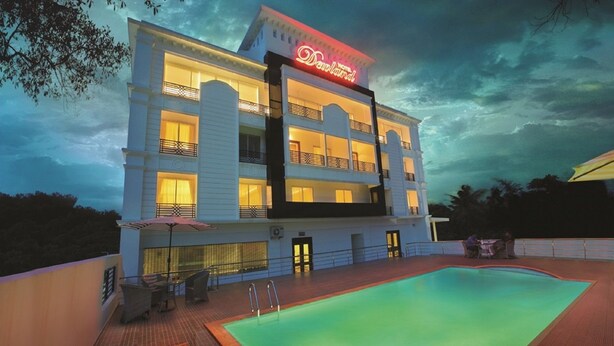 A hotel with a swimming pool, multiple balconies, and a neon sign.