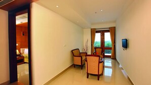 A spacious hotel corridor with a dining area, a television mounted on the wall, and a view of the outdoors through a large window.