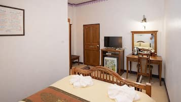 A hotel room with a bed, a desk with a chair, a television, a wardrobe, and a mirror.