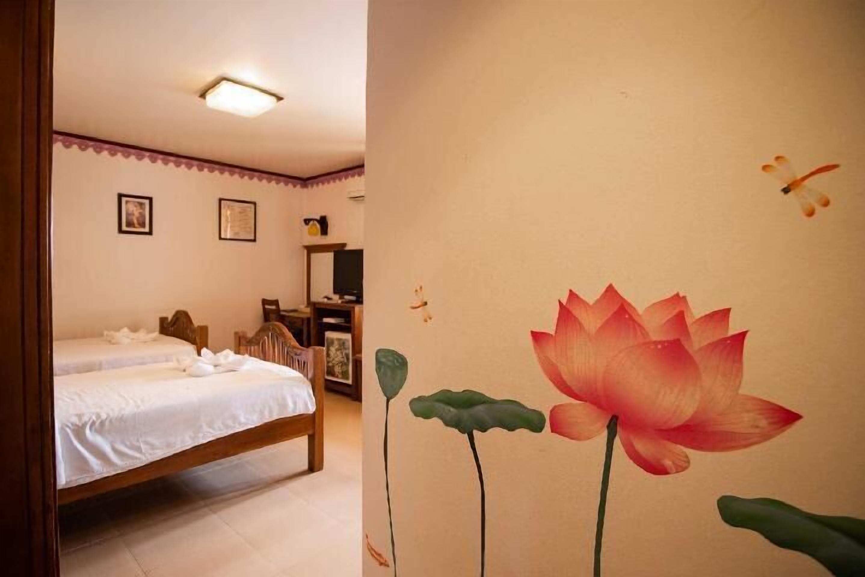 Habitación con dos camas individuales, cabecero de madera, un escritorio con silla y un mural de flor de loto en la pared.