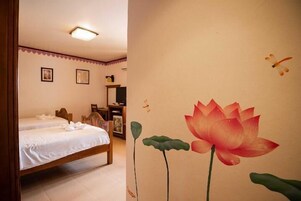 Habitación con dos camas individuales, cabecero de madera, un escritorio con silla y un mural de flor de loto en la pared.