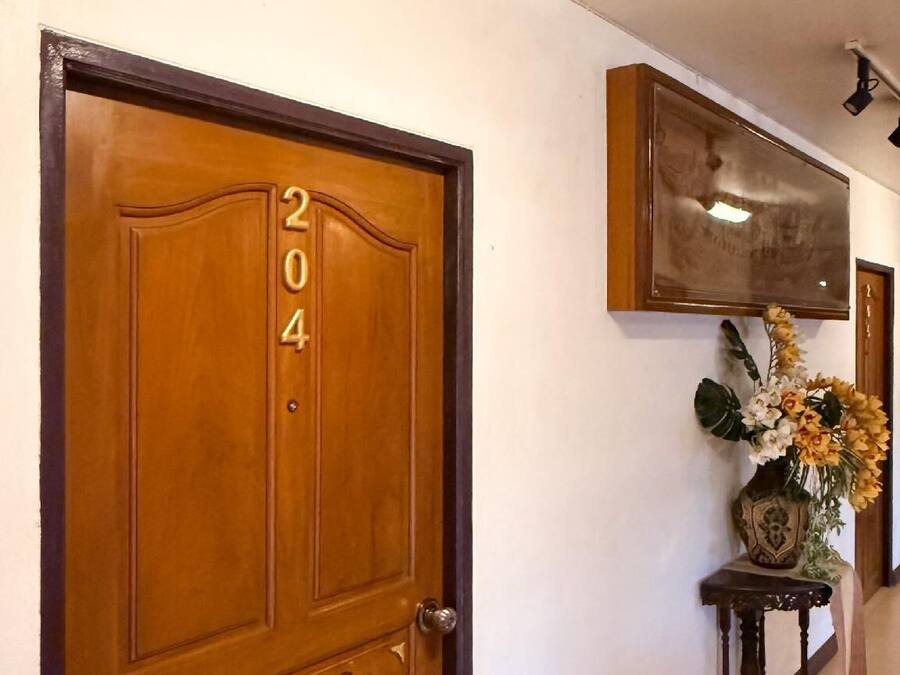 Una puerta de madera con el número 204, una mesita con un jarrón de flores y un espejo colgado en la pared.